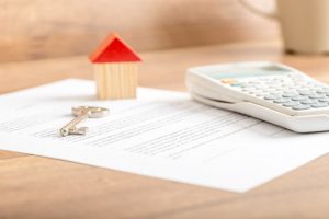 Silver house key lying on a contract for house sale, lease, insurance or mortgage in a real estate concept, viewed low angle with focus to the tip.